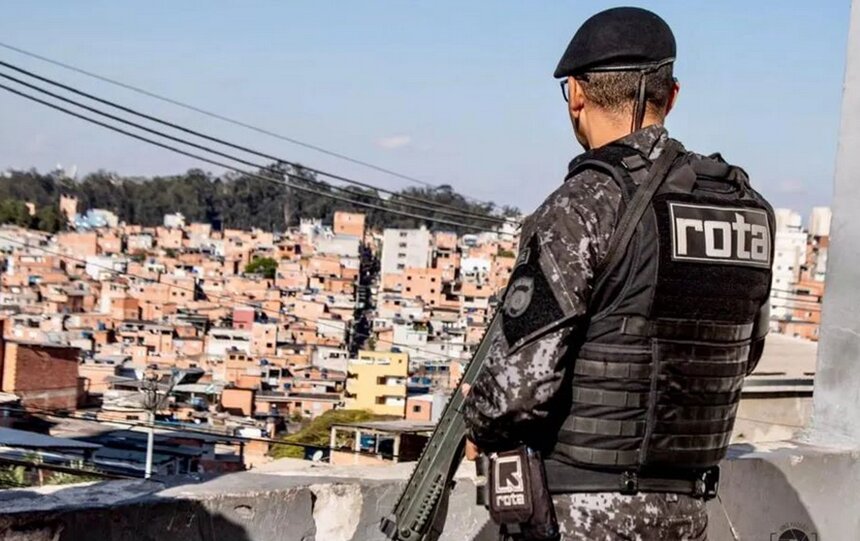 Em foto colorida policial da Rota, de costas, observa favela enquanto segura um fuzil - Metrópoles