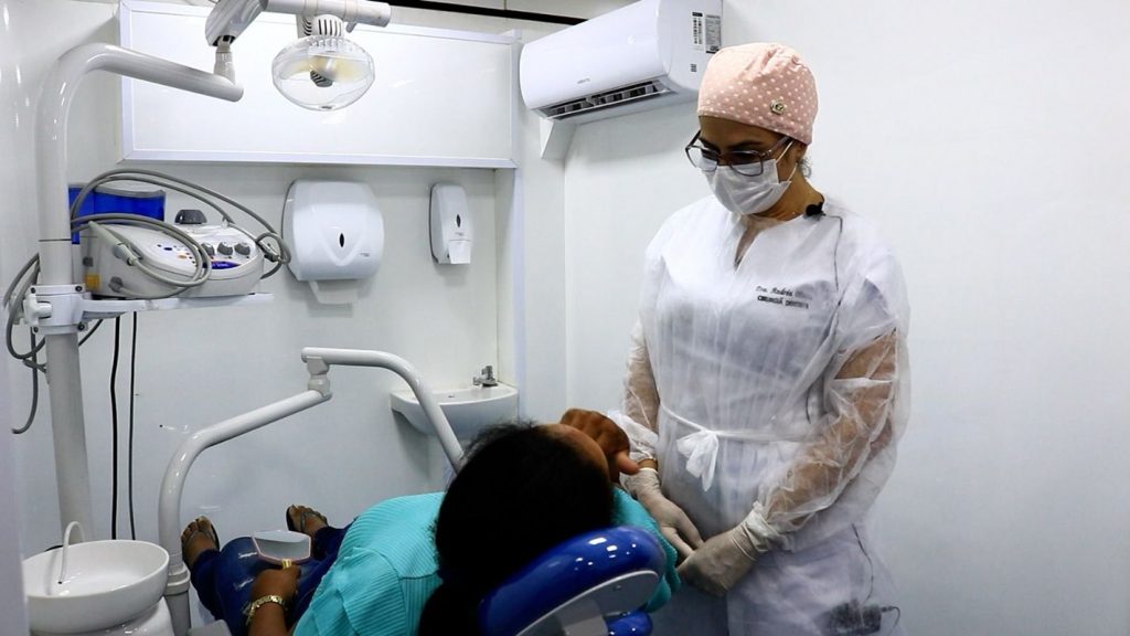 Dentista mulher atendendo paciente em consultório branco