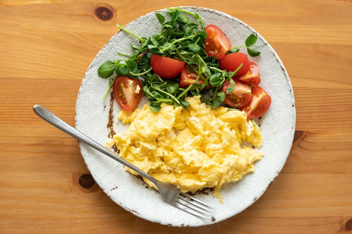 imagem colorida de um prato com ovo mexido e uma salada de tomate - Metrópoles