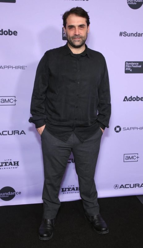Homem de roupa preta em frente a um painel lilás